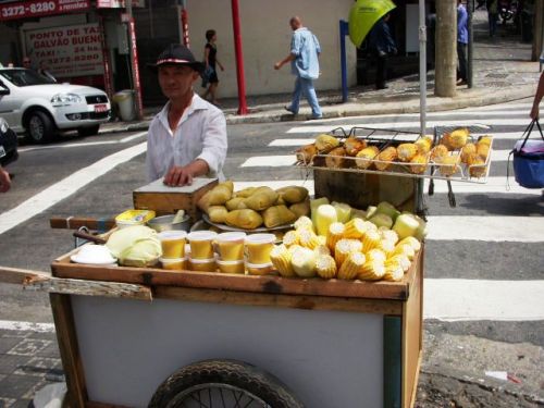 サンパウロの路上でトウモロコシ料理を販売する人。コップに入った料理がクラウ、後ろの料理がパモーニャ