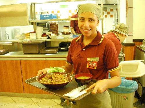 牛丼をテーブル席のお客さんに運ぶブラジル女性の従業員