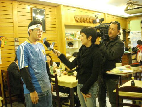 試合終了後にブラジルのテレビ局からインタビューを受ける必勝鉢巻をした店員の男性