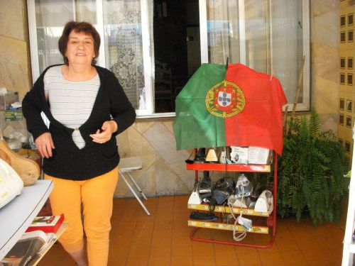 サンパウロに暮らす雑貨商のポルトガル女性と、アイロンを置いた棚の上のポルトガル国旗