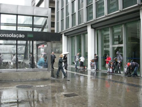 小雨の中、駅前で傘を売る人々が立っている