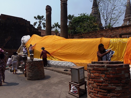 大きな涅槃仏に黄色い布を掛ける参拝者