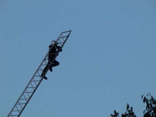 消防士が頂上の像につかまっている男性に話し掛けています