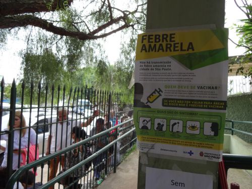 サンパウロ市の保健所で黄熱病ワクチンを受けるため屋外まで伸びた行列と施設内に貼り出された黄熱病とワクチンに関するポスター